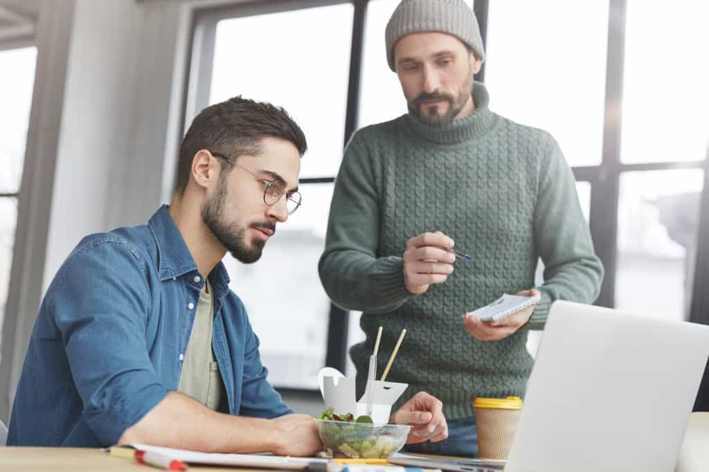 Young attractive male trainee shows presentation on laptop computer to his boss, takes into account all remarks, going to improve and add more visual effects. People, work, technology concept