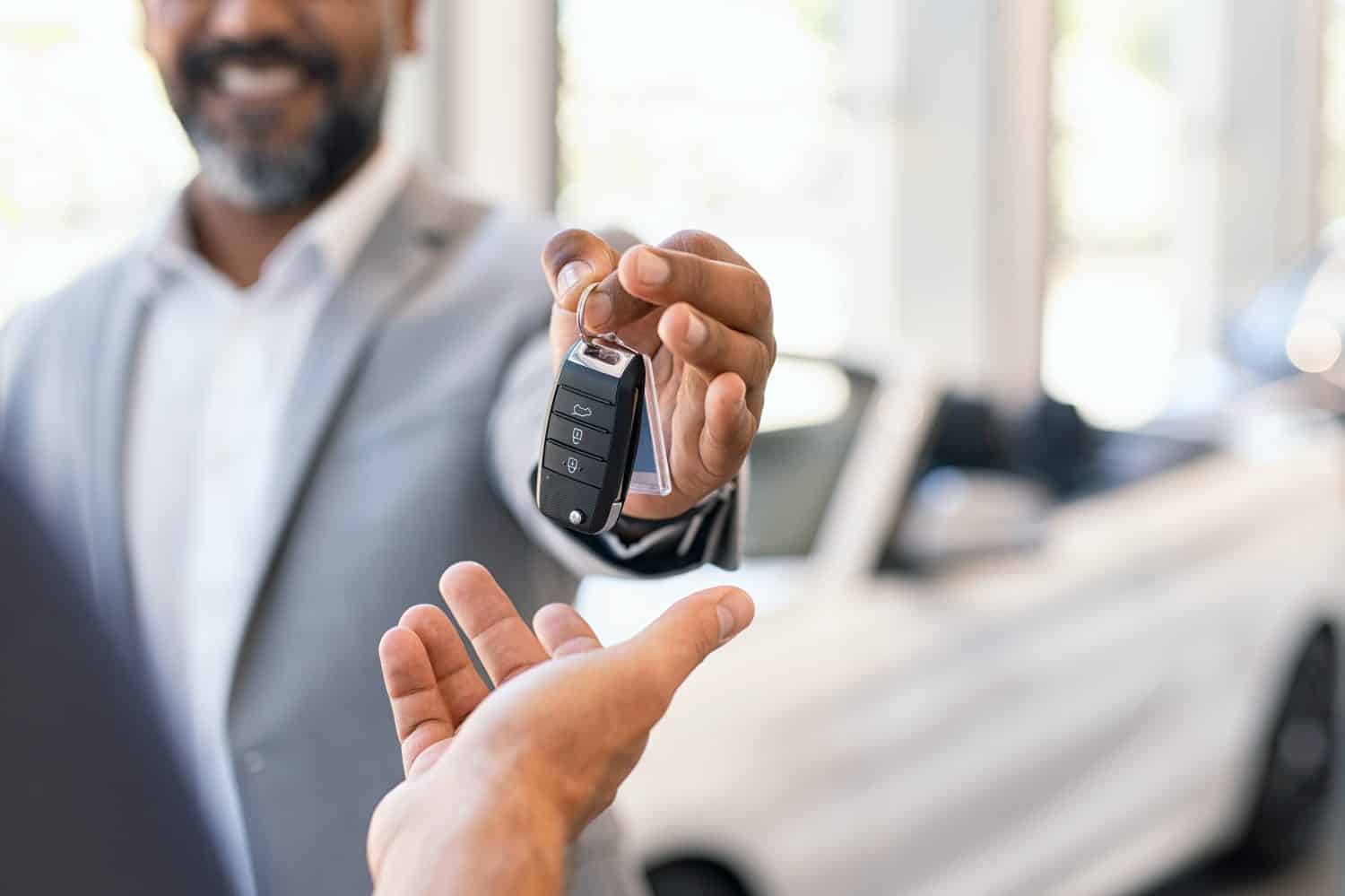 Closeup hand of cardealer giving new car key to customer. Salesman hand giving keys to a client at showroom. Man's hand receiving car keys from african agent in a auto dealership with copy space.