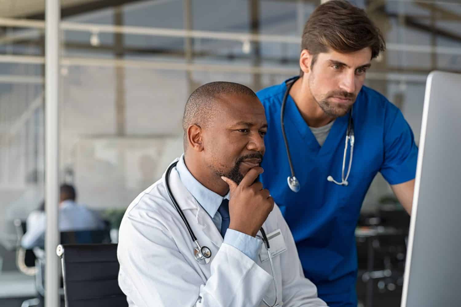 Mature african doctor and nurse analyze medical report on computer. Two healthcare workers in consultation using computer at hospital. Doctor discussing medical report with colleague at clinic.