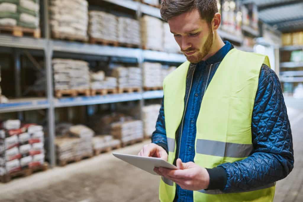 Young man shopping or working in a hardware warehouse standing checking supplies on his tablet with an absorbed expression