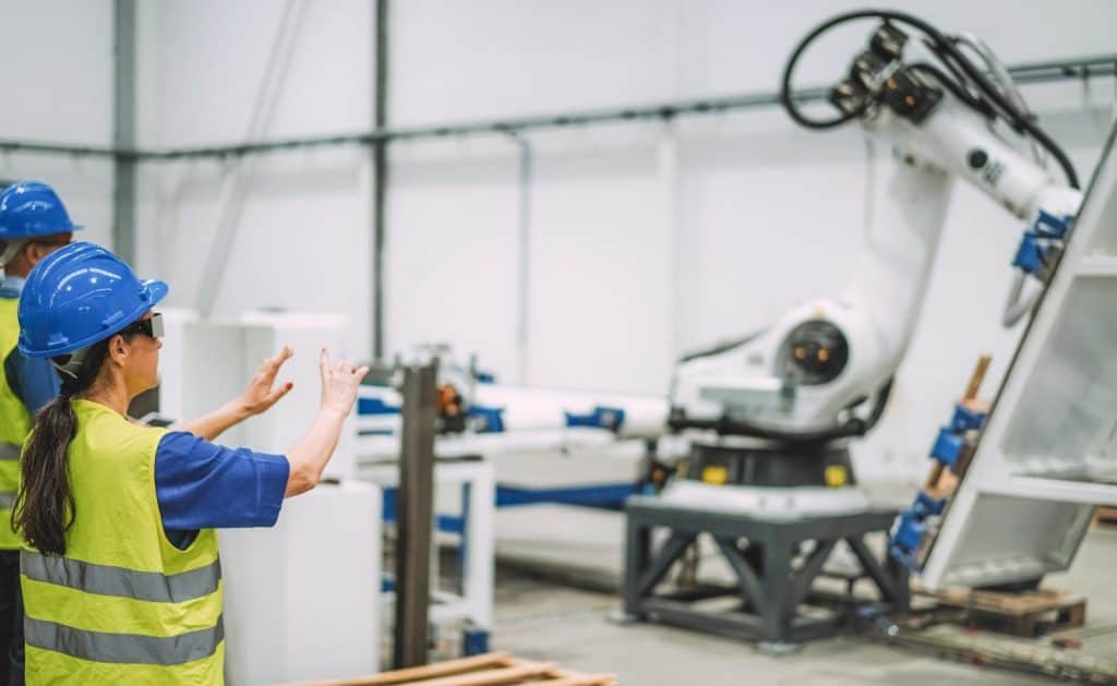 Female worker using futuristic augmented reality glasses inside robotic factory while working with ai machines - Industrial and technology concept - Focus on woman helmet