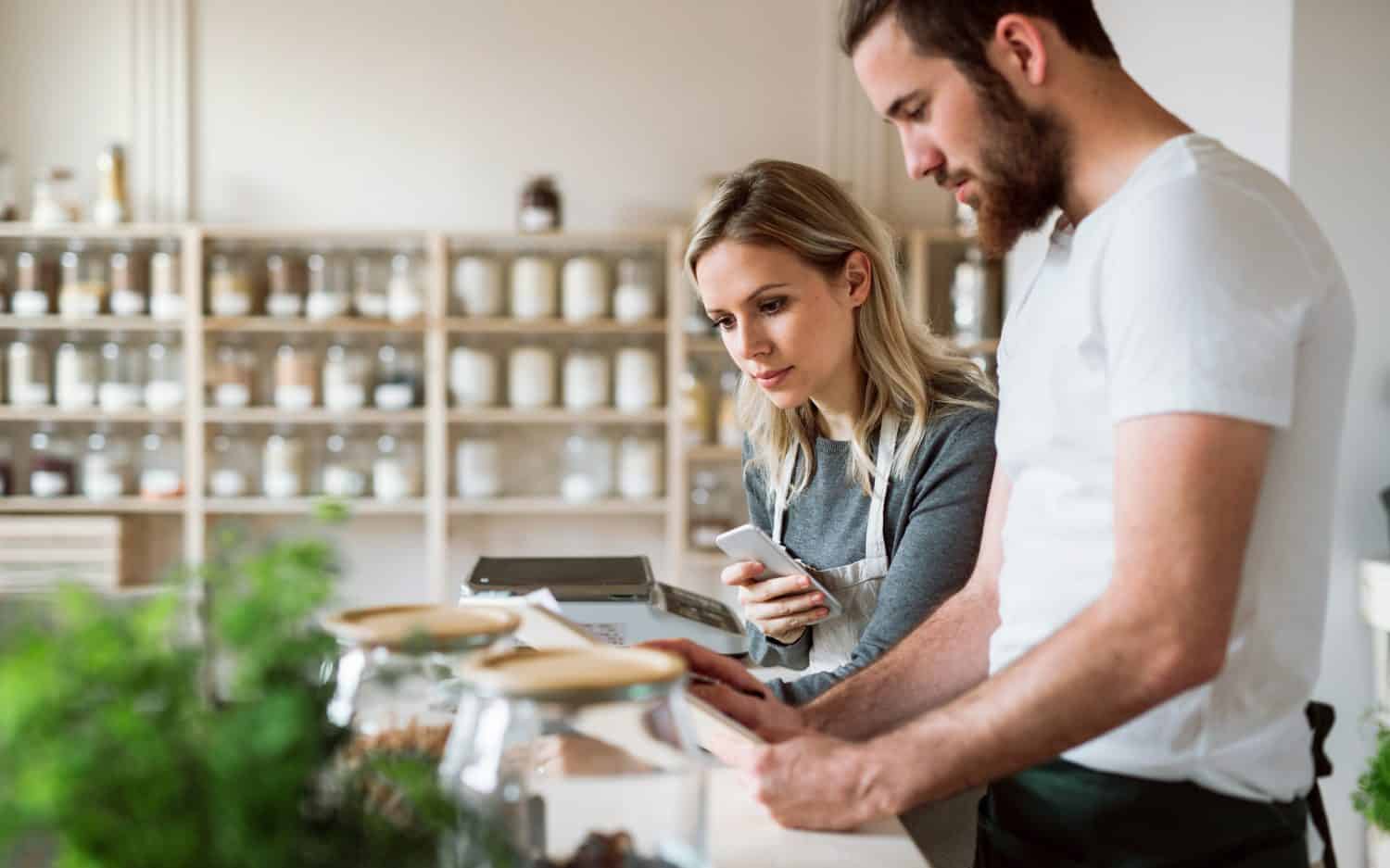 Two shop assistants standing at the counter in zero waste shop, checking stock.