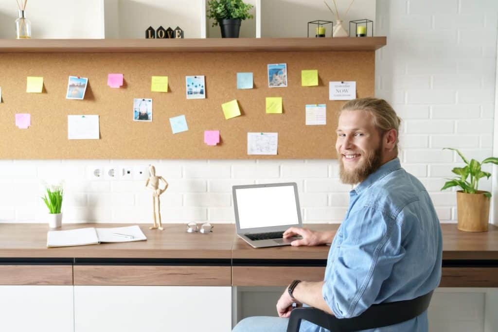 Smiling young bearded man student remote worker working studying from home office online on laptop computer sit at desk. Happy male distance freelancer professional looking at camera, portrait.