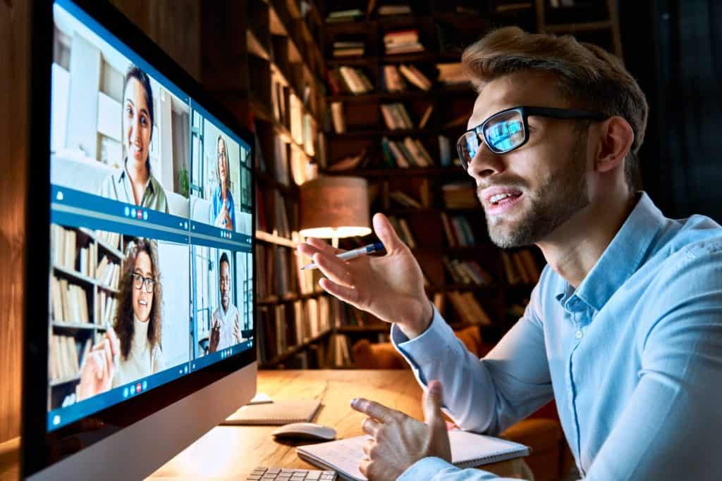 Young business man talking with diverse colleagues in virtual video conference group chat using computer at home office. Online professional videoconference communication, social distance work concept