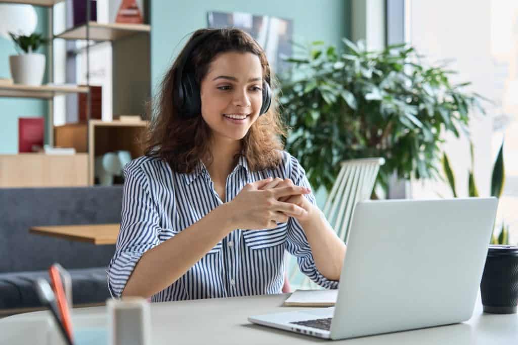 Young adult happy smiling Hispanic indian student wearing headphones talking on online chat meeting using laptop in university campus or at virtual office. College female student learning remotely.