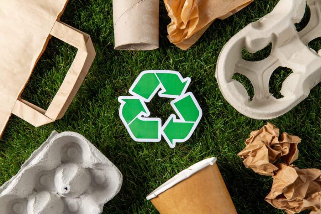 environment, sustainability and ecology concept - close up of green recycling sign and paper waste on grass