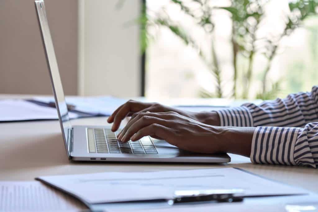 Young black female hands typing on pc keyboard. African business woman user using laptop computer working online, searching tech data in internet sitting at desk in home office. Close up view.