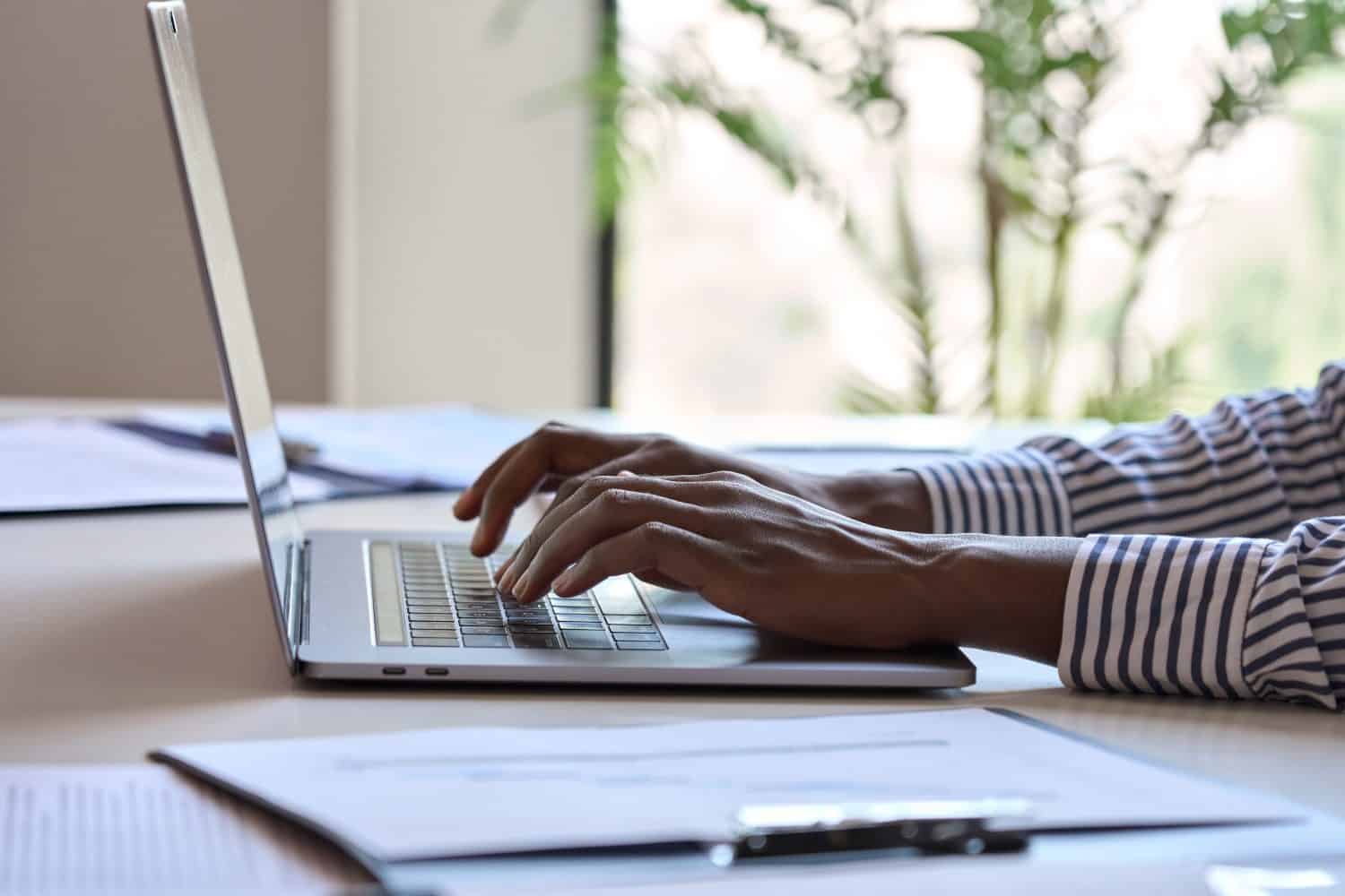 Young black female hands typing on pc keyboard. African business woman user using laptop computer working online, searching tech data in internet sitting at desk in home office. Close up view.