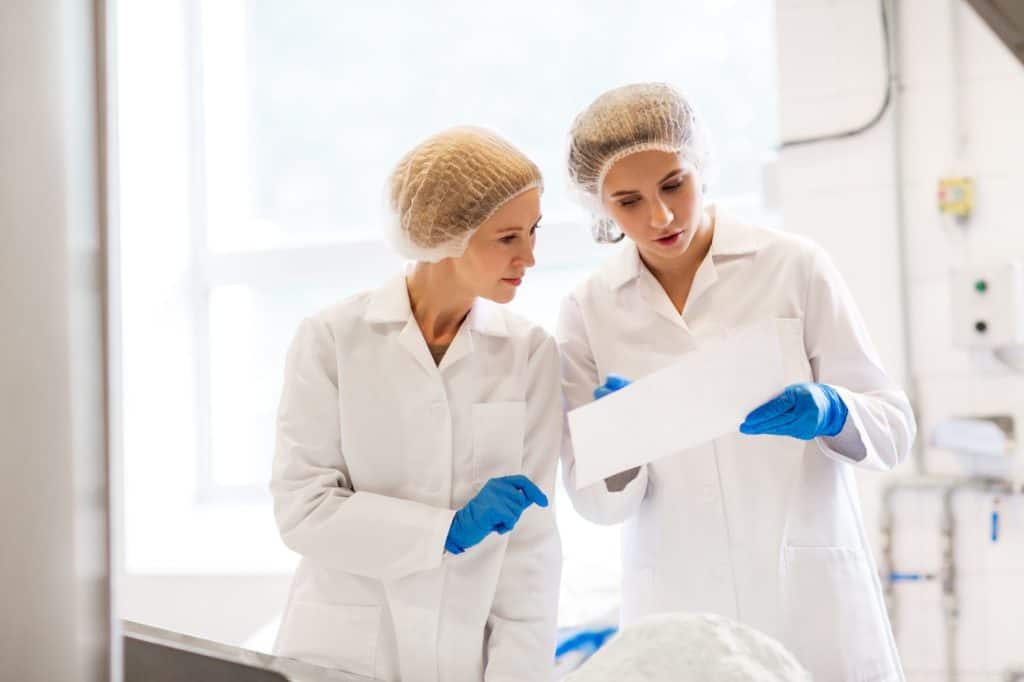 manufacture, industry, food production and people concept - women technologists with paper and powdered milk at ice cream factory shop