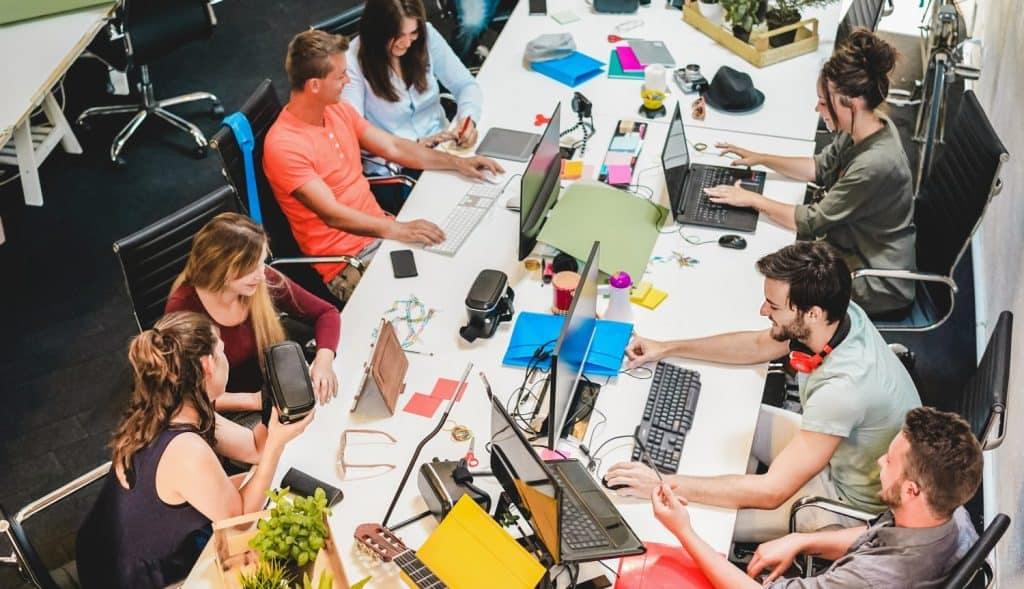 Young co-workers team talking during startup - Happy people planning a new project in creative workplace office - Technology, entrepreneur, marketing and concept - Focus on left man with headphones