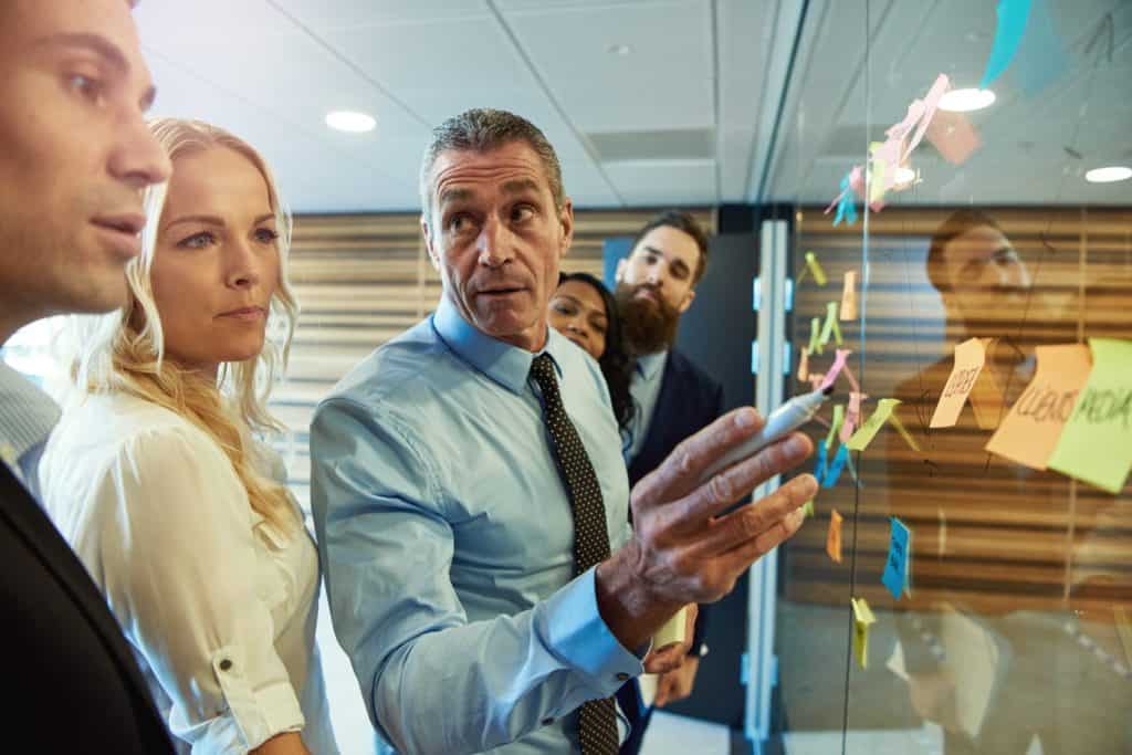 Businessman in a meeting with colleagues grouped around ideas on sticky memos looking aside with an attentive expression as he listens to a team member